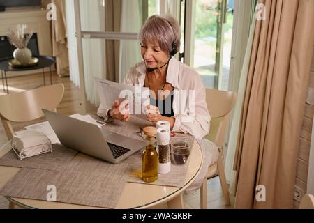 Femme communique en ligne dans sa cuisine sur un ordinateur portable Banque D'Images