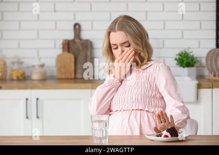 Jeune femme enceinte avec un morceau de gâteau souffrant de toxicose à table dans la cuisine Banque D'Images