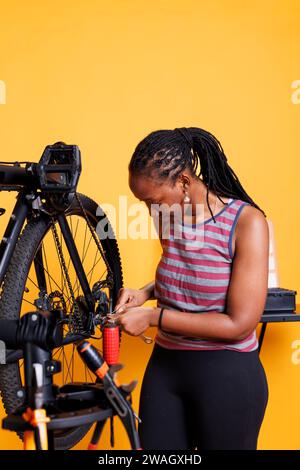 La cycliste afro-américaine ajuste et répare les composants du vélo avec une boîte à outils spécialisée, assurant des performances optimales. Femme noire sportive utilisant la clé pour le réglage de roue de vélo. Banque D'Images