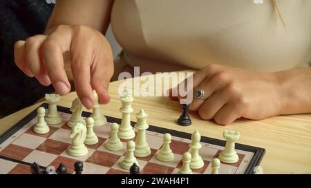 Échecs comme un jeu de cerveau, avec des pièces en noir et blanc sur le plateau. Une jeune femme est assise à la table d'échecs, faisant un mouvement. Banque D'Images