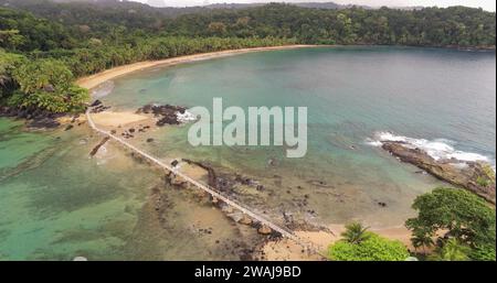 Un pont en bois pittoresque traverse un espace ouvert menant à une plage immaculée entourée d'une jungle tropicale luxuriante Banque D'Images