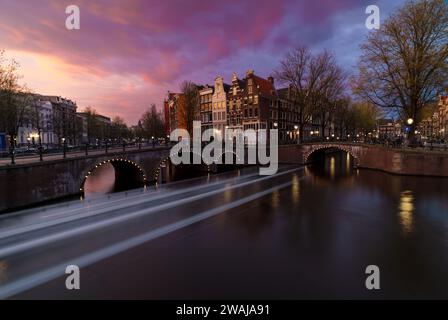 Le crépuscule se colore sur les canaux d'Amsterdam avec des ponts historiques et des maisons sous un ciel de coucher de soleil vibrant Banque D'Images