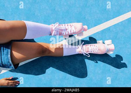 D'en haut des jambes féminines anonymes dans des chaussettes blanches et des baskets quad roller s'installant sur un terrain de sport de couleur bleue avec de l'ombre sur une journée ensoleillée Banque D'Images