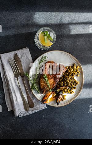D'en haut le steak de saumon BBQ assaisonné avec des épices accompagné de câpres fermentées, citron carbonisé, une branche de romarin, avec une eau de citron rafraîchissante sur Banque D'Images