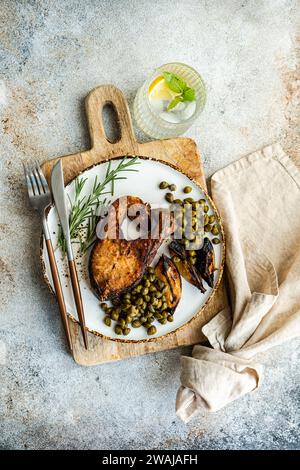 Vue de dessus du steak de saumon grillé sain assaisonné avec des épices à côté de citrons rôtis et câpres sur une planche de bois avec une serviette en lin et de l'eau de citron Banque D'Images