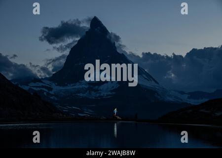 Une scène tranquille au crépuscule avec des silhouettes au bord d'un lac de montagne réfléchissant sous un sommet majestueux Banque D'Images