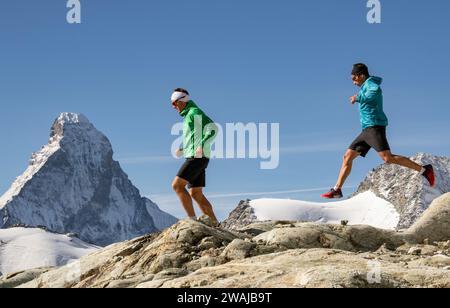Vue latérale de deux coureurs en jogging sportswear sur une crête de haute montagne avec des sommets enneigés au loin Banque D'Images