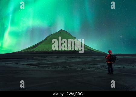 Vue arrière d'une personne méconnaissable se tenant devant un volcan sous les dynamiques aurores boréales en Islande Banque D'Images