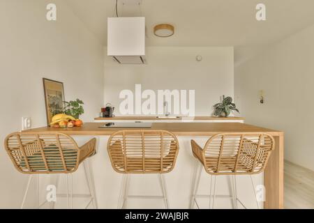 Induction et fruits sur l'île en bois avec des chaises vides dans la cuisine moderne de luxueux appartement avec des murs blancs Banque D'Images