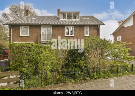 Plantes vertes par clôture contre maison de mur en brique détachée avec balcon et fenêtres dans le quartier Banque D'Images