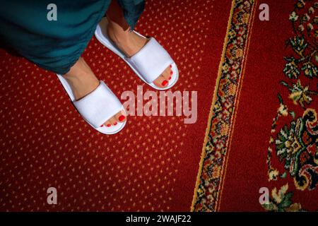 Une femme portant des pantoufles de spa debout sur un tapis à motifs complexes dans un hôtel luxueux Banque D'Images