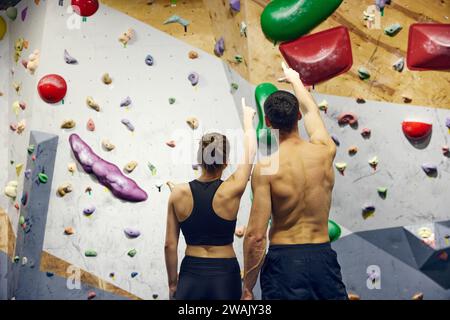 Jeune homme et femme, athlètes regardant sur le mur d'escalade, discutant des techniques d'entraînement. École de blocs Banque D'Images