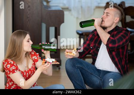 Une fille et son petit ami sur un rendez-vous assis à la maison, manger de la pizza et boire de la bière. Banque D'Images