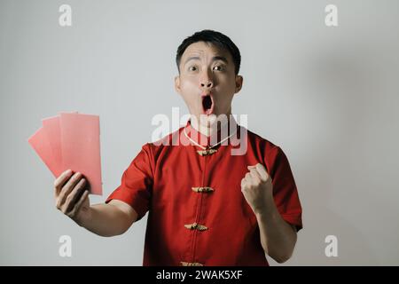 Visage heureux de l'homme asiatique portant Cheongsam ou tissu traditionnel chinois tout en tenant angpao sur fond blanc. Gong Xi Fa Cai. Banque D'Images