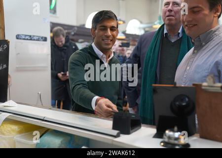 Le Premier ministre Rishi Sunak (à gauche) et Sir Graham Brady (deuxième à droite) commandent de la nourriture à la Great Northern Pie Company lors d'une visite au marché alimentaire d'Altrincham dans le Grand Manchester. Date de la photo : Vendredi 5 janvier 2024. Banque D'Images