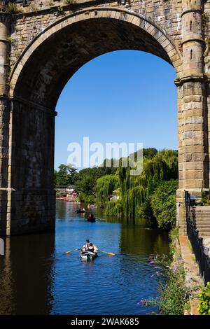 Touristes en bateaux à rames loués sur la rivière Nidd avec le viaduc ferroviaire, Pateley Bridge. Knaresborough, Yorkshire, Angleterre Banque D'Images