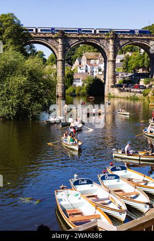 Touristes en location bateaux à rames sur la rivière Nidd, avec un train passant sur le viaduc ferroviaire, Pateley Bridge.Knaresborough, Yorkshire, Angleterre Banque D'Images