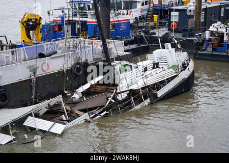 Le bateau Bar & Co, qui est amarré à Temple Pier, sort de l'eau après le bateau de fête de Londres, qui sert de bar flottant, de restaurant et de discothèque, coulé dans la Tamise. L'impact des eaux de surface et des inondations fluviales continuera d'être « significatif » dans certaines parties de l'Angleterre suite aux fortes pluies, ont averti les experts. Date de la photo : Vendredi 5 janvier 2024. Banque D'Images