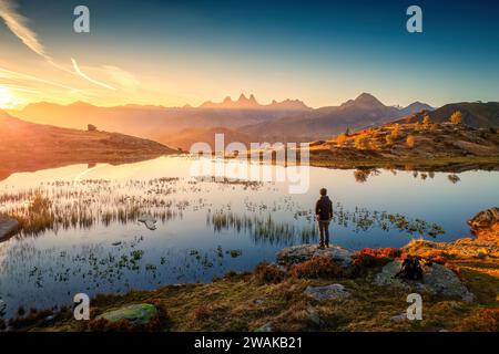 Paysage des Alpes françaises de lever du soleil brille sur le lac Guichard avec massif des Arves, randonneur mâle debout en automne aux aiguilles d'Arves, Savoie, France Banque D'Images