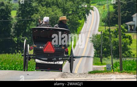 Une vue arrière d'un couple Amish dans un cheval ouvert et buggy sur une route rurale Banque D'Images