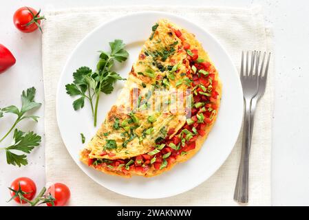 Omelette farcie avec poivron rouge et oignon vert sur plaque sur fond de pierre clair. Vue de dessus, pose à plat Banque D'Images