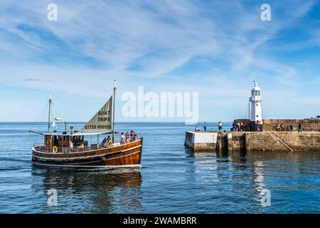 Mevagissey, Cornouailles, Royaume-Uni - 16 août 2023 : le phare et l'entrée du port à Mevagissey sur la côte sud de Cornouailles. Un bateau touristique arrive Banque D'Images