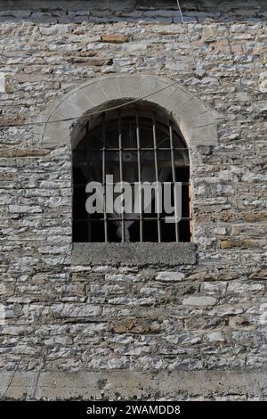 213 fenêtre barrée d'arc rond et tableau arrière, rideau blanc plié à l'intérieur, bâtiment dans le secteur de la Tour de l'horloge. Gjirokaster-Albanie. Banque D'Images