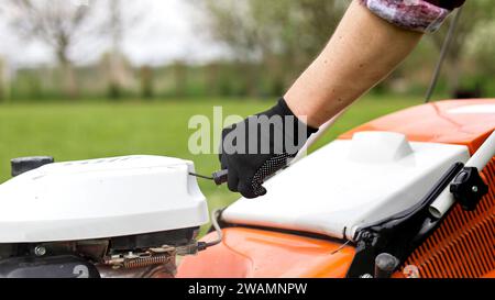 Un jardinier méconnaissable en gants de protection démarre le robot de tonte avant de couper de l'herbe verte dans son jardin. Homme avec tondeuse à gazon motorisé env Banque D'Images