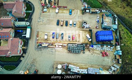 Vue aérienne d'un chantier de construction avec des matériaux et des véhicules, entouré de bâtiments. Banque D'Images