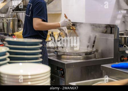 Cuisine animée d'un restaurant de ramen bouillant le bouillon à des nouilles habilement conçues, cette scène incarne la maîtrise culinaire et le dévouement à l'auten Banque D'Images