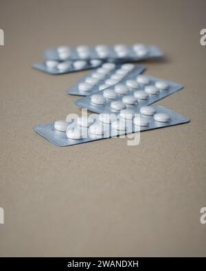 comprimés de couleur blanche éparpillés dans des blisters, médicaments pour les allergies, antibiotiques, analgésiques, emballages pour comprimés isolés sur brun Banque D'Images