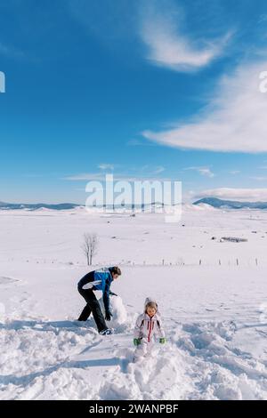 Petite fille et son père font un bonhomme de neige en roulant de grosses boules de neige sur la pelouse Banque D'Images