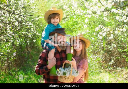 Une famille joyeuse pique-nique dans un parc. Agriculteurs familiaux travaillant dans le jardin des arbres au printemps. Père mère et enfant travaillent dans la cour avec des outils de jardinier. Banque D'Images