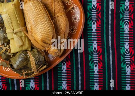 Différents tamales dans un plat en argile sur une nappe aux couleurs du drapeau mexicain. Banque D'Images