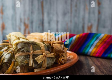 Différents tamales dans un plat en argile sur une table en bois avec un sérape coloré. Banque D'Images