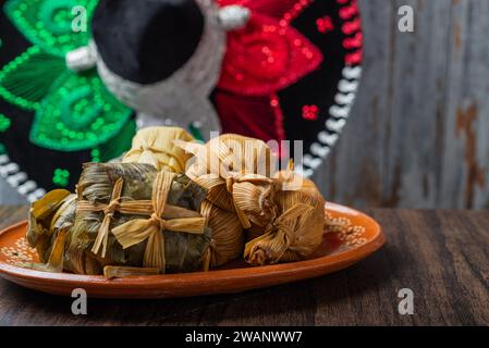 Différents tamales dans un plat en argile sur une table en bois. Fond avec chapeau mariachi. Banque D'Images