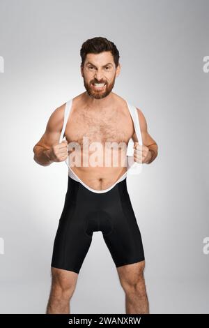 Lutteur barbu en colère en singlet noir et blanc, tout en posant à la caméra. Vue de face de l'athlète agressif faisant face, montrant la rage, isolé sur fond de studio blanc. Concept de lutte. Banque D'Images