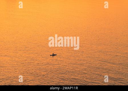 Les gens aventureux sur une planche de stand up paddle pagaie pendant un lever de soleil lumineux et vibrant Banque D'Images