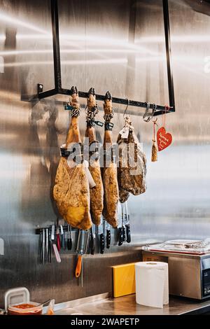 Jambons séchés suspendus dans une délicatessen espagnole. Des jambons traditionnels espagnols sont suspendus au-dessus d'un étalage de couteaux, dans une épicerie fine spécialisée. Varsovie Banque D'Images