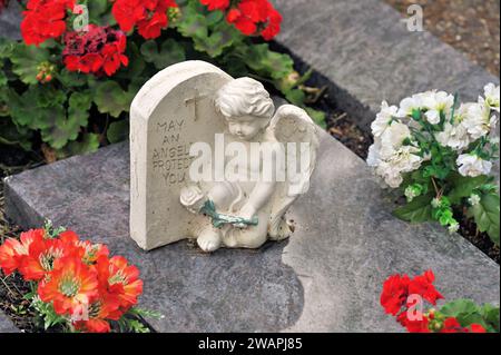 Ange grave avec inscription 'May an Angel Protect you' repose sur une dalle de granit entourée de fleurs Banque D'Images