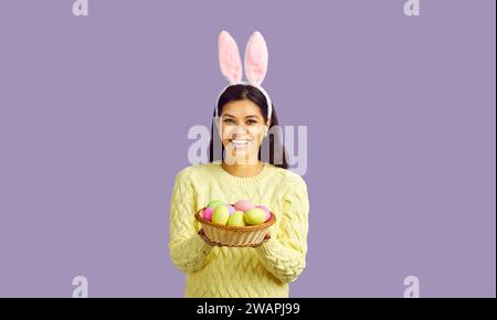 Portrait de studio de jeune femme heureuse dans les oreilles mignonnes de lapin tenant le bol des oeufs de Pâques Banque D'Images