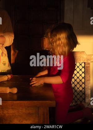 Vue de dessus de table verticale d'une fille aux cheveux blonds jouant avec la pâte sur la table sa mère debout près dans une cuisine de campagne italienne pendant le Go Banque D'Images