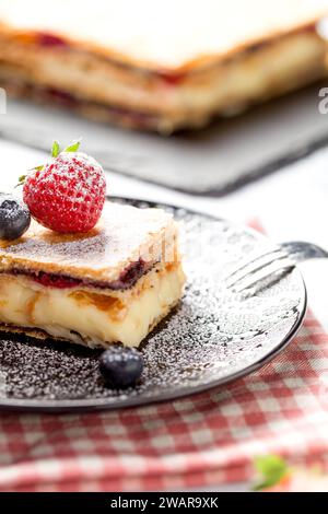 Un morceau de gâteau Napoléon aux graines de pavot et aux cerises, décoré de fraises et de bleuets sur un fond clair. Gros plan Banque D'Images