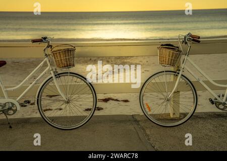 Deux vélos se dessinent dans le décor d'un coucher de soleil orange et rose éclatant sur la plage Banque D'Images