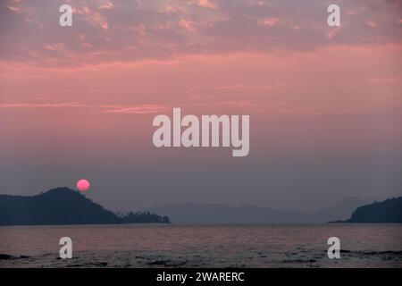 Un magnifique coucher de soleil avec un ciel rose sur un plan d'eau tranquille, avec des affleurements rocheux le long du rivage, créant un paysage pittoresque Banque D'Images