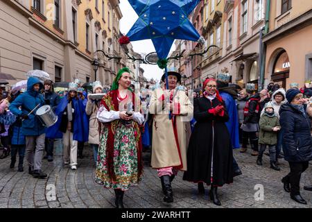 Une foule, portant des couronnes de papier et des vêtements régionaux suivent un homme avec une étoile alors qu'ils participent à une pièce de la Nativité publique jouée dans la rue de la vieille ville de Cracovie, en Pologne, le 6 janvier 2024. Le 6 janvier est la fête des trois rois polonais, lorsque des célébrations de masse ont lieu et que le jeu de la Nativité est joué par les acteurs avec les membres du public. Les célébrations ont le caractère d'une fête familiale. Plus de 800 villes ont joué la pièce en Pologne cette année. Des centaines de personnes ont assisté au festival malgré le temps froid et pluvieux. Banque D'Images