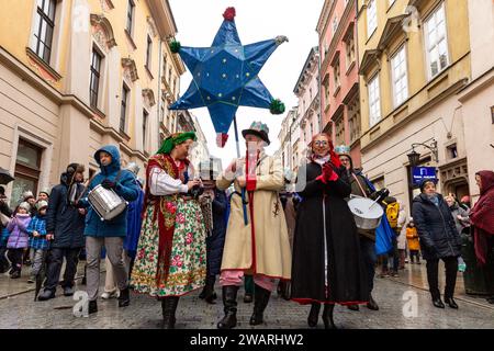 Une foule, portant des couronnes de papier et des vêtements régionaux suivent un homme avec une étoile alors qu'ils participent à une pièce de la Nativité publique jouée dans la rue de la vieille ville de Cracovie, en Pologne, le 6 janvier 2024. Le 6 janvier est la fête des trois rois polonais, lorsque des célébrations de masse ont lieu et que le jeu de la Nativité est joué par les acteurs avec les membres du public. Les célébrations ont le caractère d'une fête familiale. Plus de 800 villes ont joué la pièce en Pologne cette année. Des centaines de personnes ont assisté au festival malgré le temps froid et pluvieux. Banque D'Images