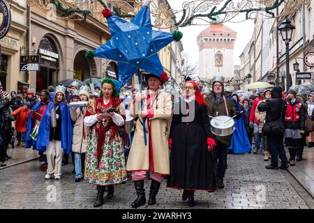 Une foule, portant des couronnes de papier et des vêtements régionaux suivent un homme avec une étoile alors qu'ils participent à une pièce de la Nativité publique jouée dans la rue de la vieille ville de Cracovie, en Pologne, le 6 janvier 2024. Le 6 janvier est la fête des trois rois polonais, lorsque des célébrations de masse ont lieu et que le jeu de la Nativité est joué par les acteurs avec les membres du public. Les célébrations ont le caractère d'une fête familiale. Plus de 800 villes ont joué la pièce en Pologne cette année. Des centaines de personnes ont assisté au festival malgré le temps froid et pluvieux. Banque D'Images