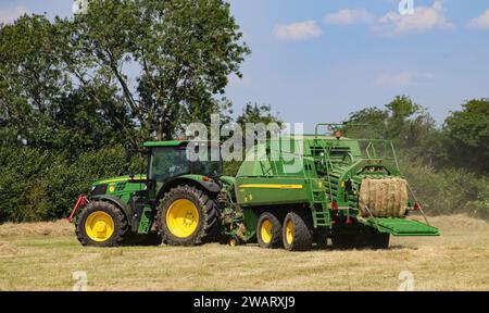 Tracteur John Deere 6155R avec une presse à balles L1534 dans la campagne du Wiltshire par une journée d'été ensoleillée. Banque D'Images