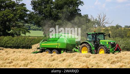 Tracteur John Deere 6155R avec une presse à balles L1534 dans la campagne du Wiltshire par une journée d'été ensoleillée. Banque D'Images